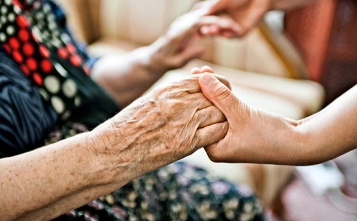 Eine jüngere Hand hält die Hand eines älteren Menschen